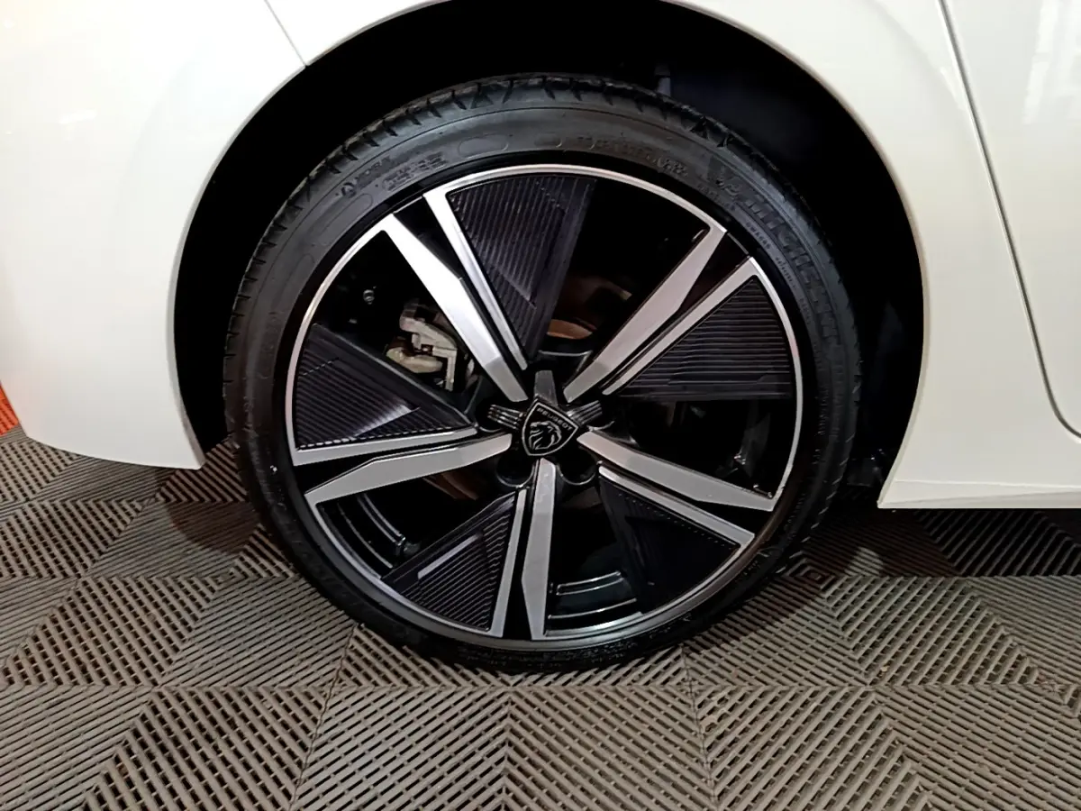 Gros plan sur la roue avant gauche de la Peugeot 308 PHEV 180 E-EAT8 GT blanche, avec jante alliage noire et argentée.