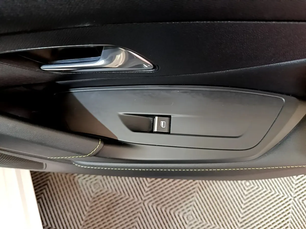 Détail de la commande de lève-vitre côté gauche sur la porte intérieure noire d'une Peugeot 308 PHEV 180 E-EAT8 GT blanche.