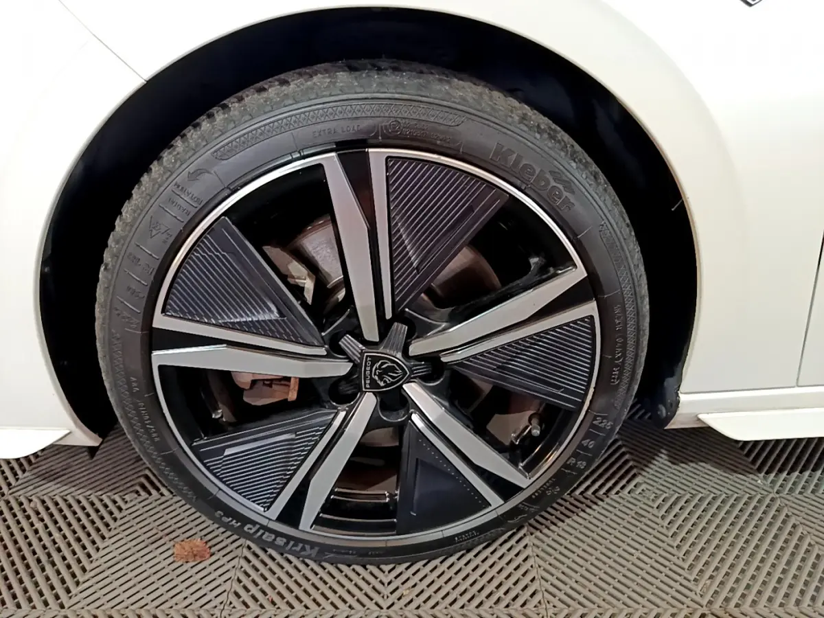 Gros plan sur la roue avant gauche d'une Peugeot 308 PHEV 180 GT blanche avec jante alliage noire et argentée.