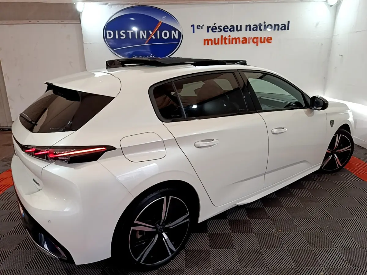 Peugeot 308 PHEV 180 GT blanc vue 3/4 arrière droit avec toit ouvrant et feux arrière LED allumés.