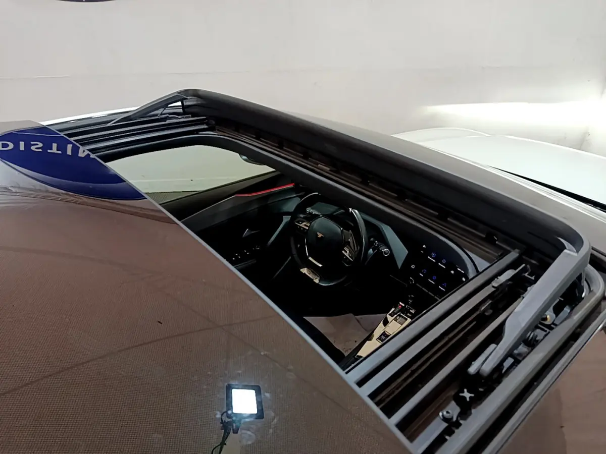 Vue plongeante sur l'intérieur noir du Peugeot 308 PHEV blanc 2022 via toit ouvrant panoramique ouvert.