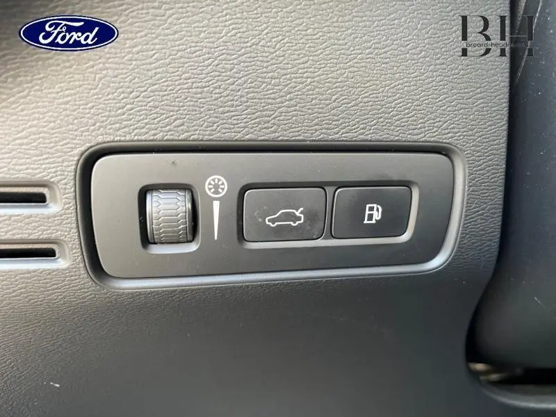 Gros plan sur les commandes noires du tableau de bord du Volvo XC40 gris Glacier, avec bouton ouverture coffre et réservoir.