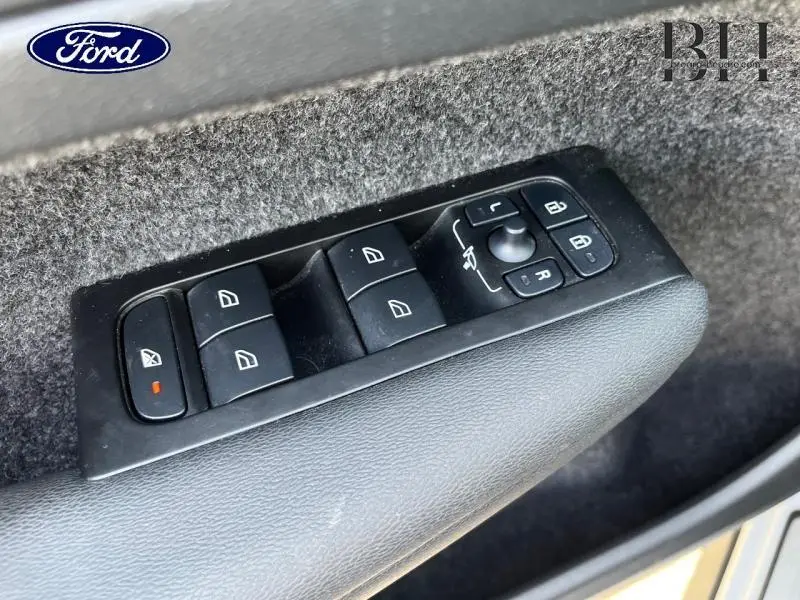 Panneau de commandes des vitres et rétroviseurs côté conducteur en plastique noir, sur porte intérieure grise.