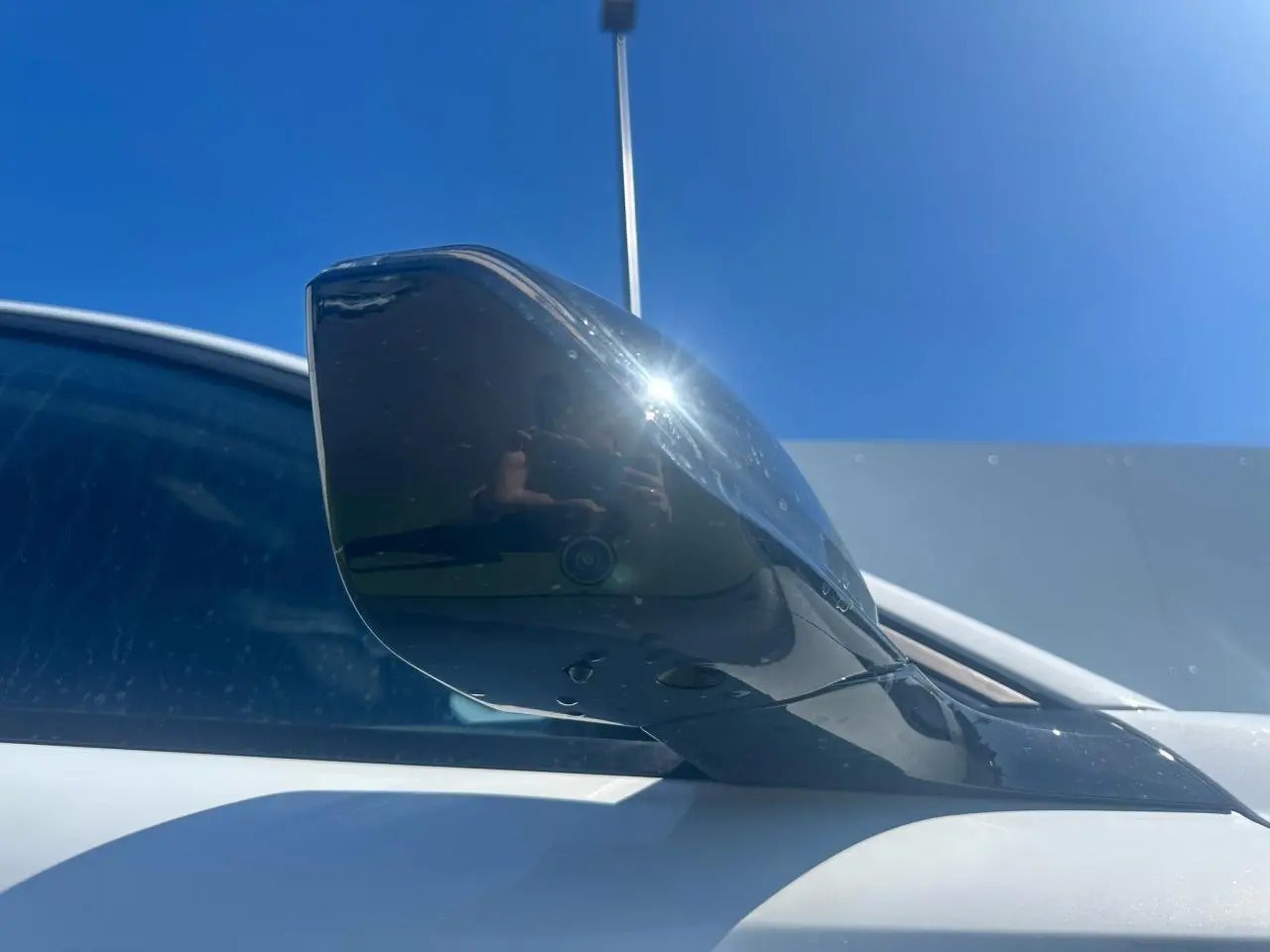 Rétroviseur droit noir brillant sur Peugeot 308 blanc Okenite sous un ciel bleu lumineux.