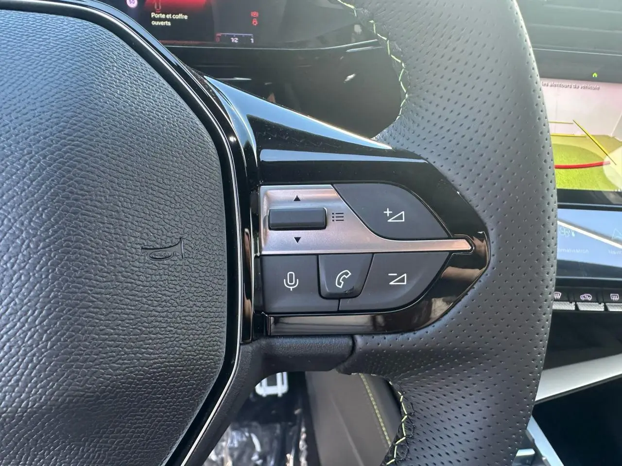 Gros plan sur les commandes du volant cuir perforé de la Peugeot 308 blanche, avec écran tactile en arrière-plan.