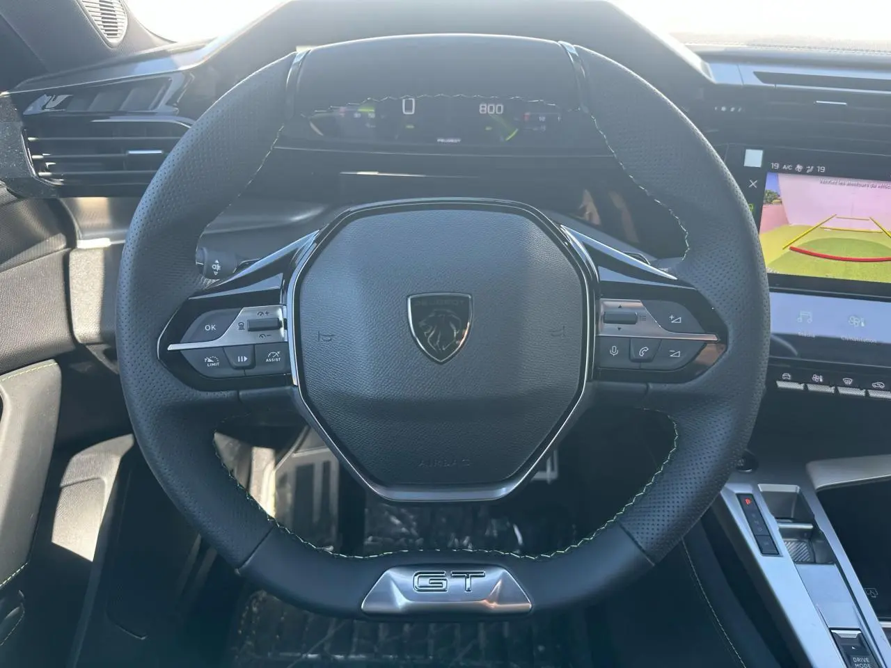Volant cuir noir GT de Peugeot 308 2025 vu de face, avec commandes intégrées et combiné numérique en arrière-plan.
