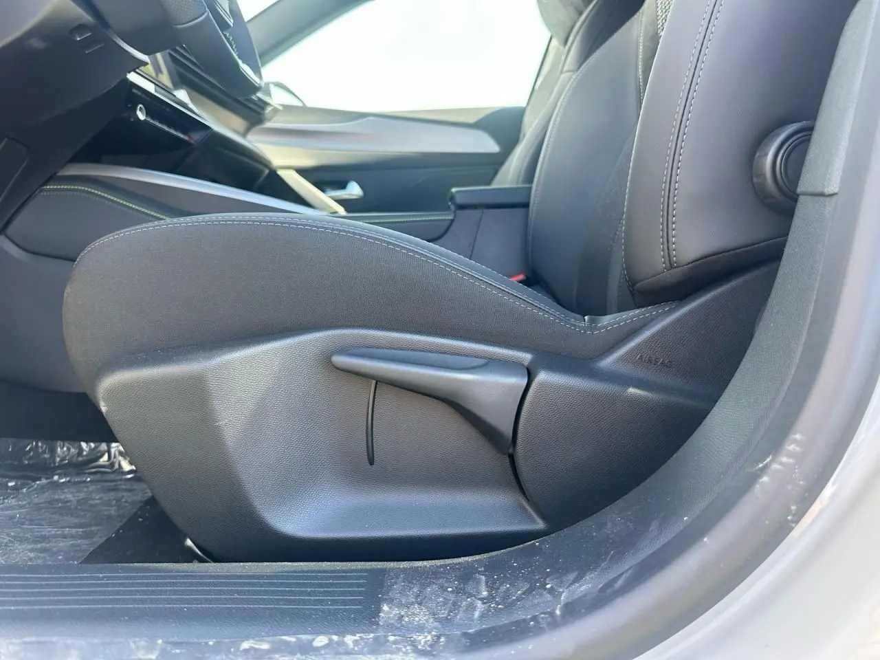 Gros plan sur le siège avant côté conducteur de la Peugeot 308 blanche Okenite, intérieur noir avec coutures visibles.