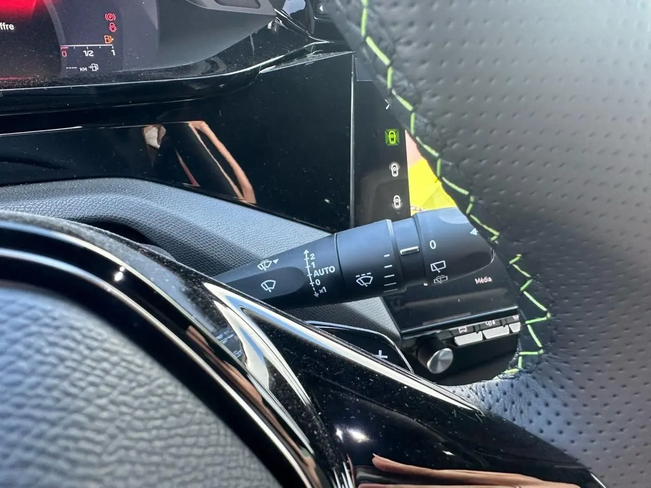 Détail du commodo d'essuie-glace et volant cuir perforé avec surpiqûres vertes dans le Peugeot 308 blanc Okenite 2025.