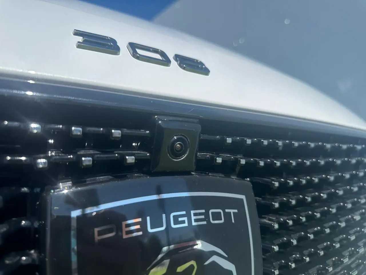 Gros plan sur la calandre noire brillante et la caméra avant d'une Peugeot 308 blanche avec logo et monogramme 308.