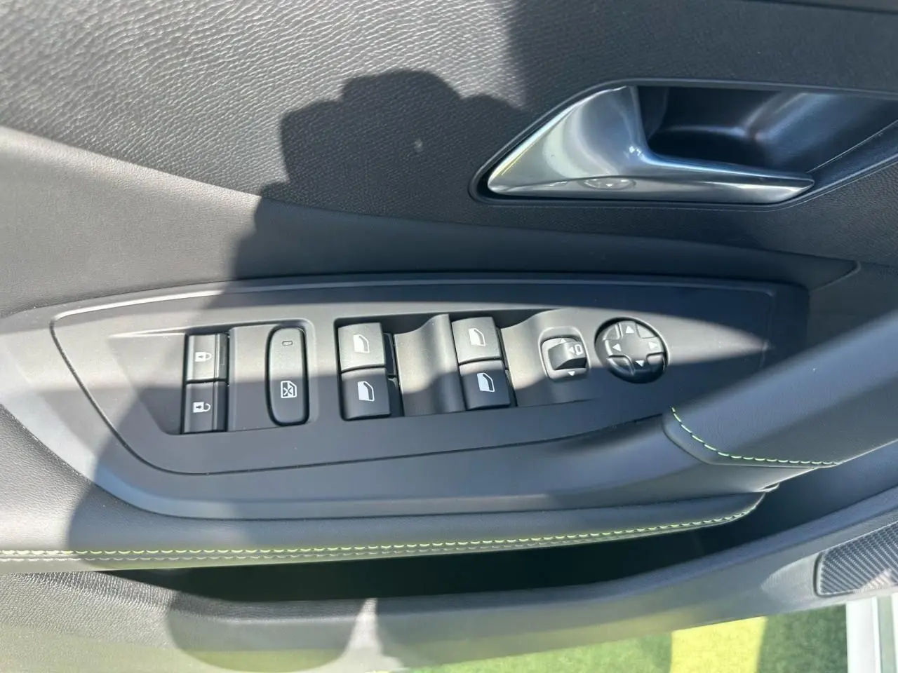 Gros plan sur la commande des vitres et rétroviseurs côté gauche, garniture noire avec surpiqûres vertes.