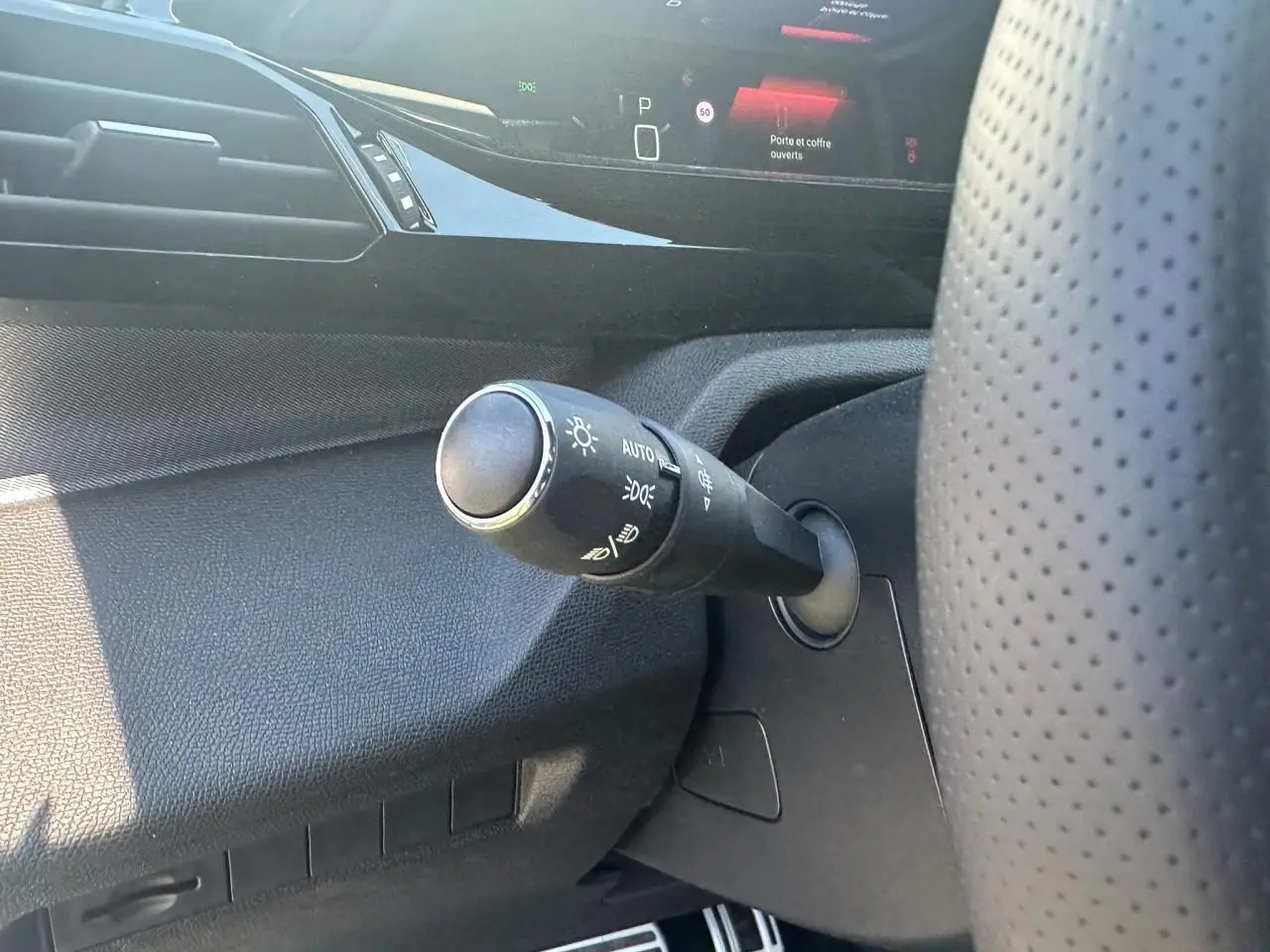 Gros plan sur la commande des feux à gauche du volant perforé dans l'habitacle noir de la Peugeot 308 2025.
