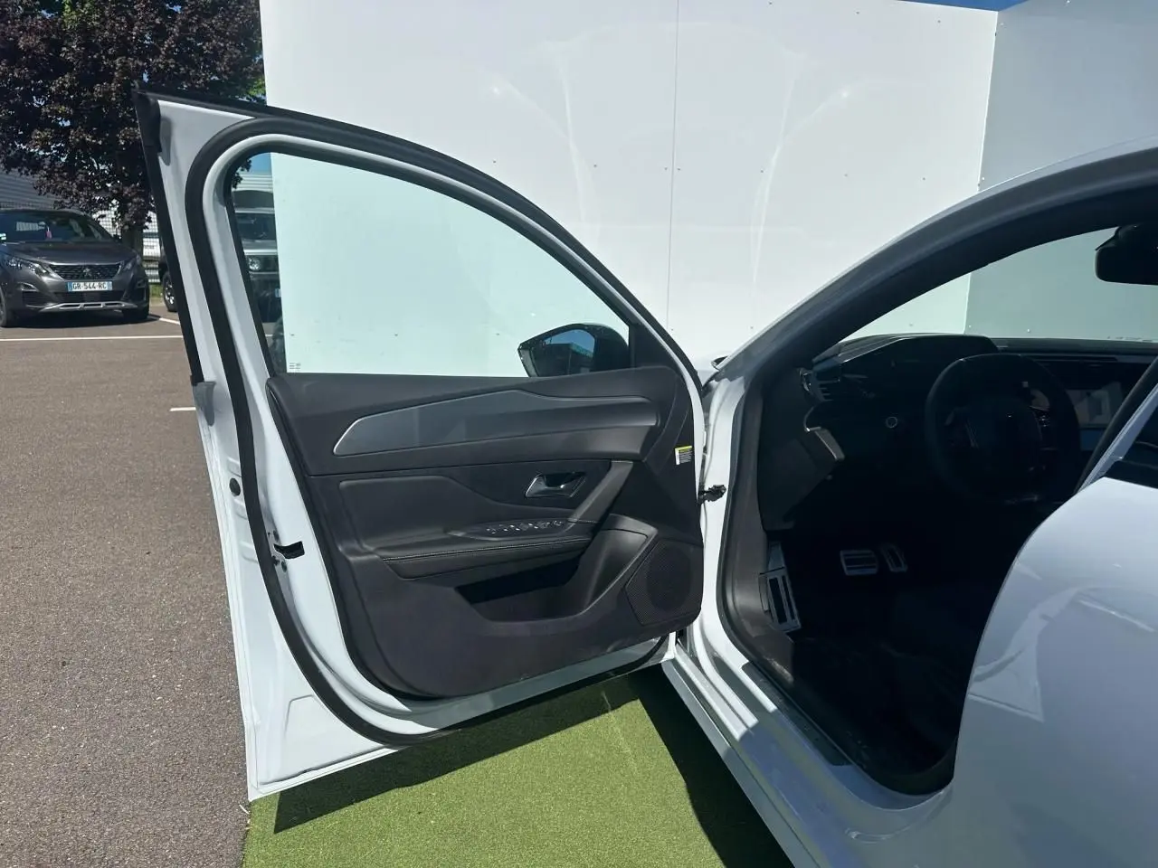 Portière avant gauche ouverte d'une Peugeot 308 blanche, montrant l'intérieur noir et le tableau de bord partiel.