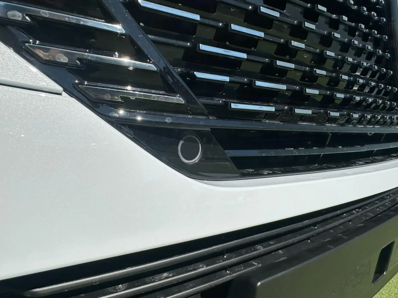 Gros plan sur la calandre noire brillante et la partie avant blanche nacrée d'une Peugeot 308 2025.