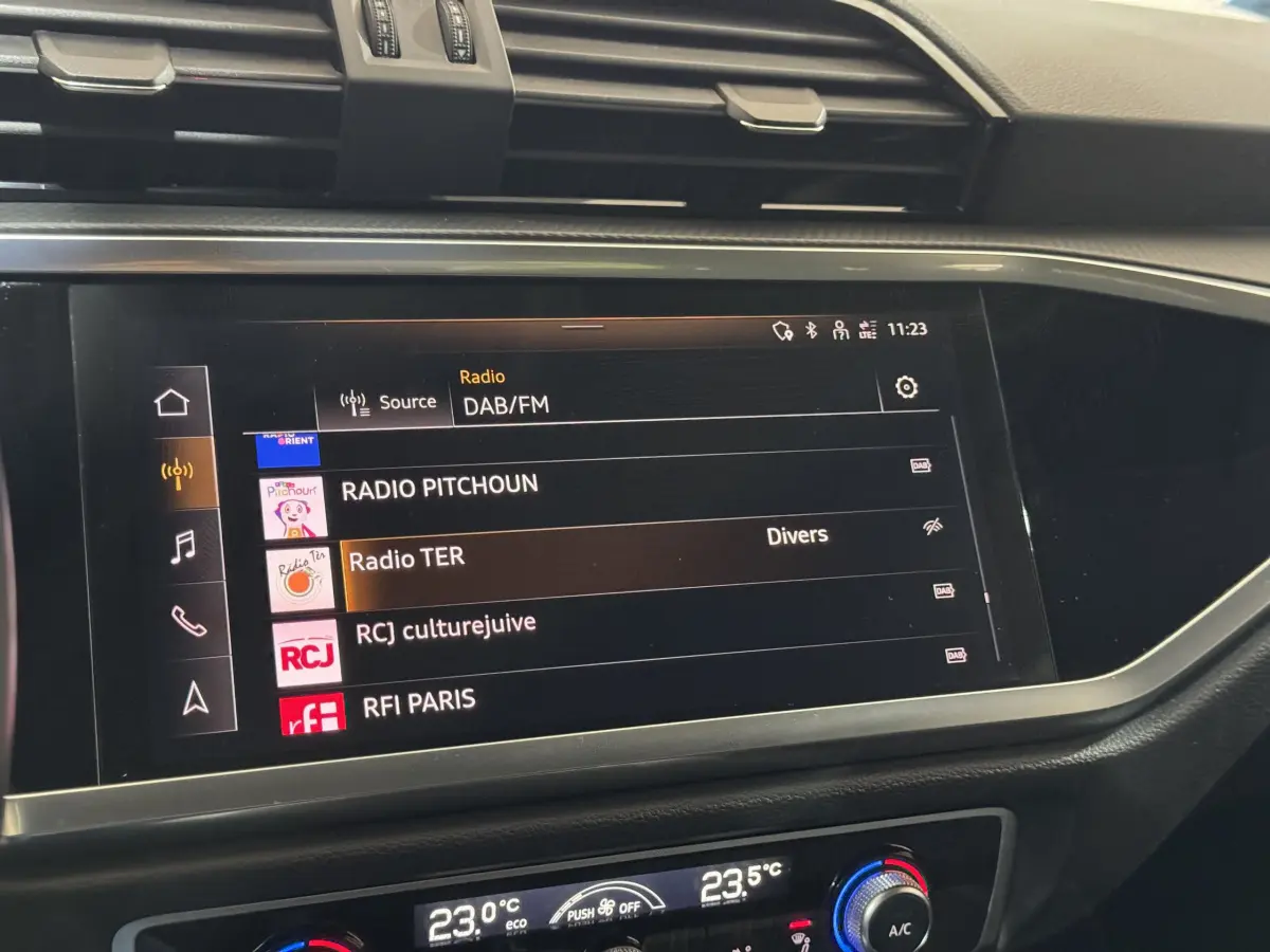 Écran tactile central de l’Audi Q3 noir 2022 affichant les stations radio DAB/FM avec commandes climatisation digitales.