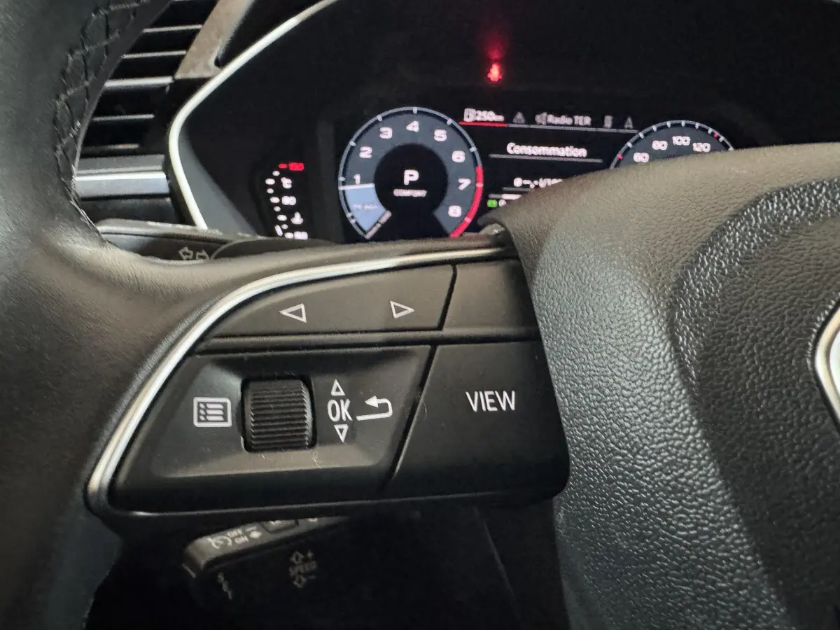 Gros plan sur les commandes gauche du volant noir d’un Audi Q3 35 TFSI 2022 avec tableau de bord numérique en arrière-plan.