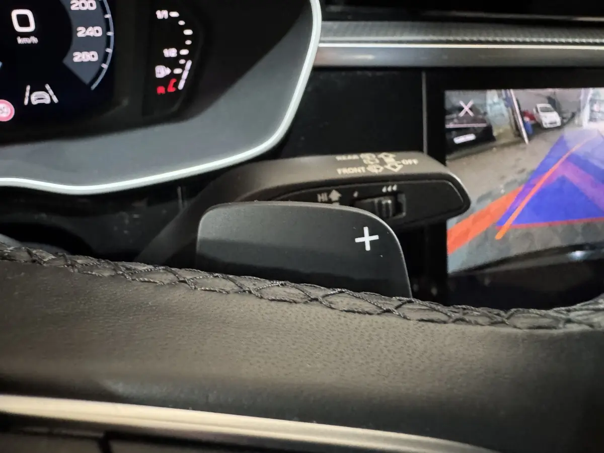 Gros plan sur la palette de changement de vitesse droite du volant cuir noir d’un Audi Q3, avec affichage caméra de recul visible.