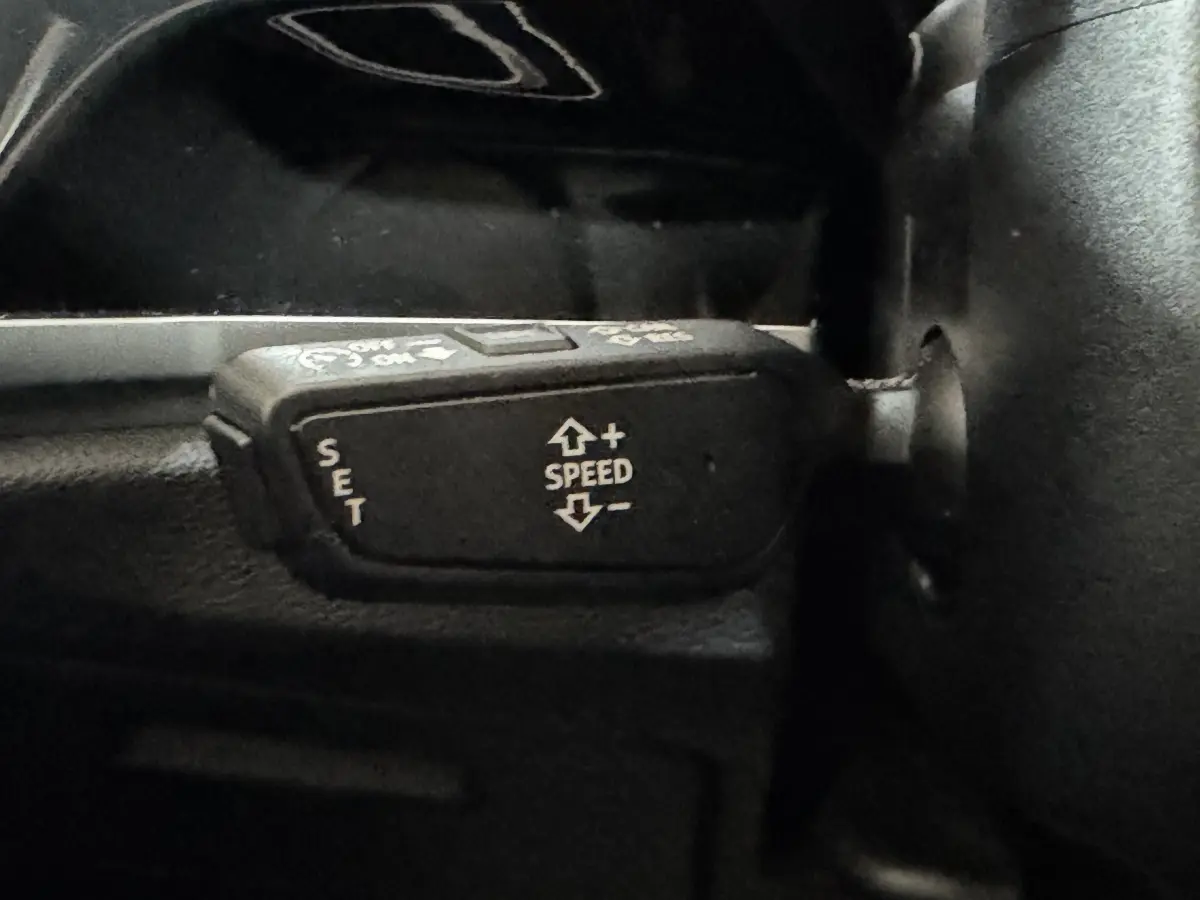 Gros plan sur la commande de régulateur de vitesse noir dans l’Audi Q3 35 TFSI 2022, intérieur sombre.