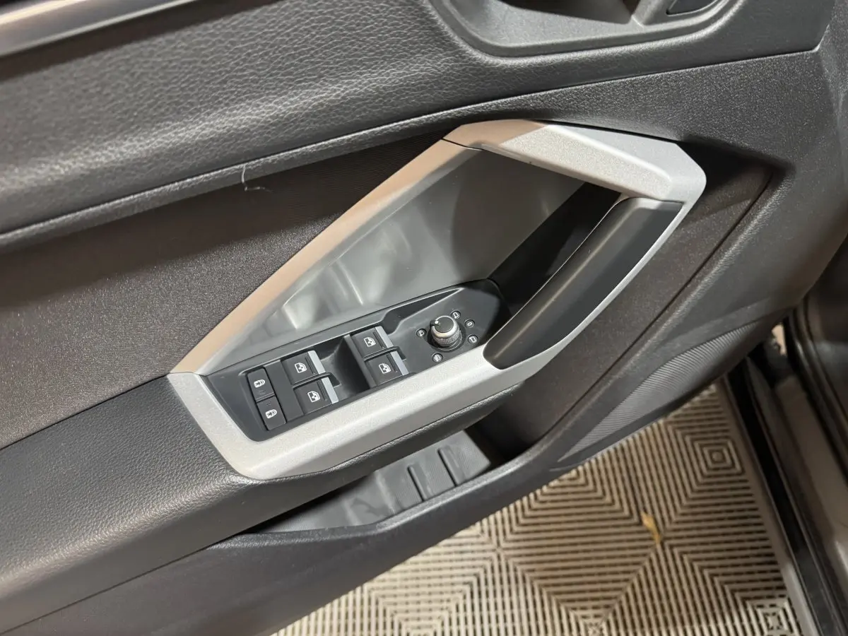 Gros plan sur la commande des vitres et rétroviseurs côté conducteur de l'Audi Q3 noir, avec cadre argenté.