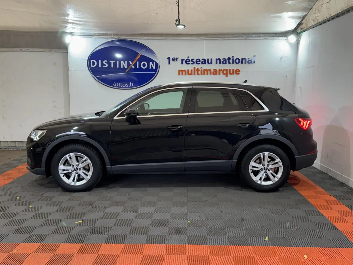 Audi Q3 noir vue de profil côté gauche dans un showroom avec éclairage intérieur et logo Distinxion en arrière-plan.