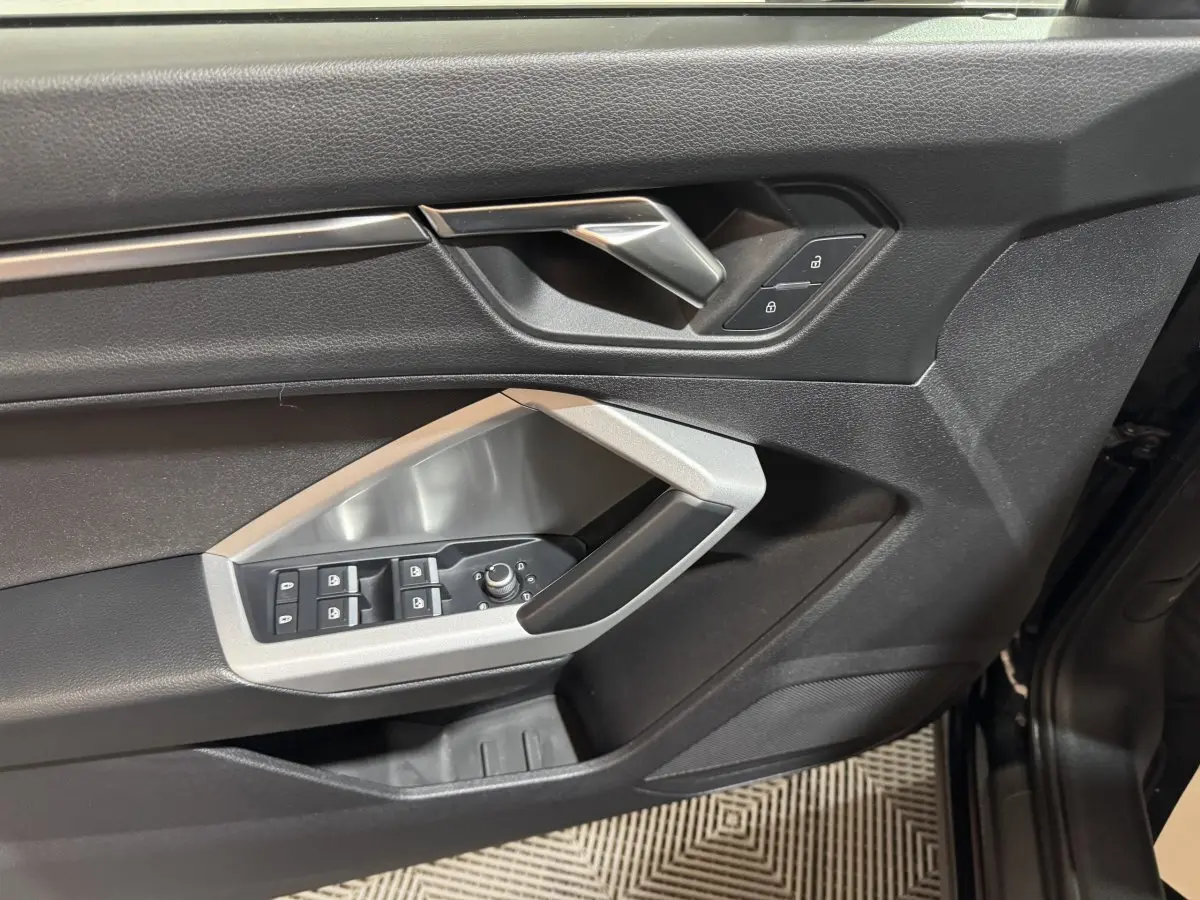Vue rapprochée de la porte avant gauche noire de l’Audi Q3 35 TFSI avec commandes de vitres et verrouillage.