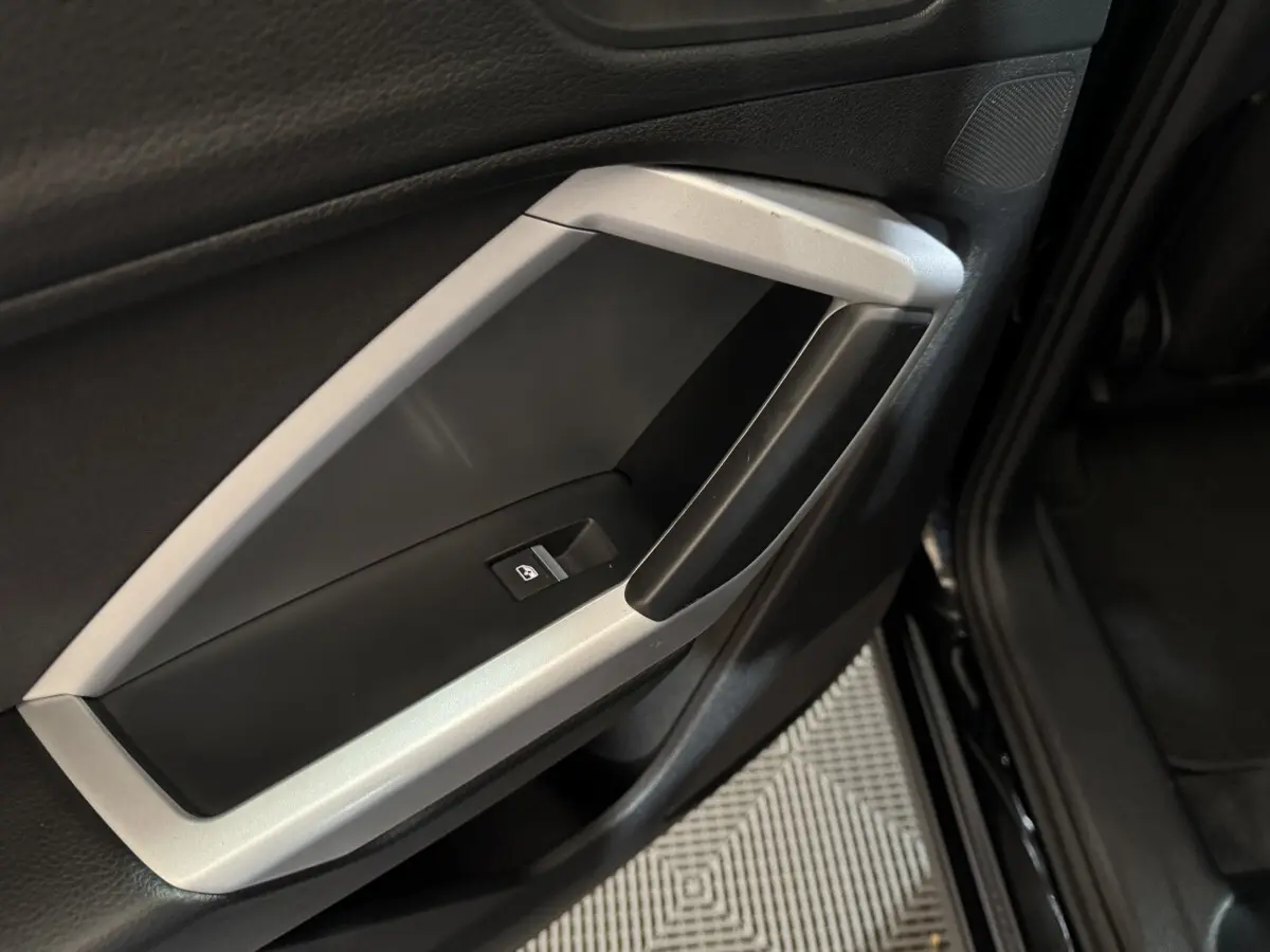 Gros plan sur la poignée intérieure côté gauche de la porte noire d’un Audi Q3 35 TFSI 2022 avec bouton de commande de vitre.