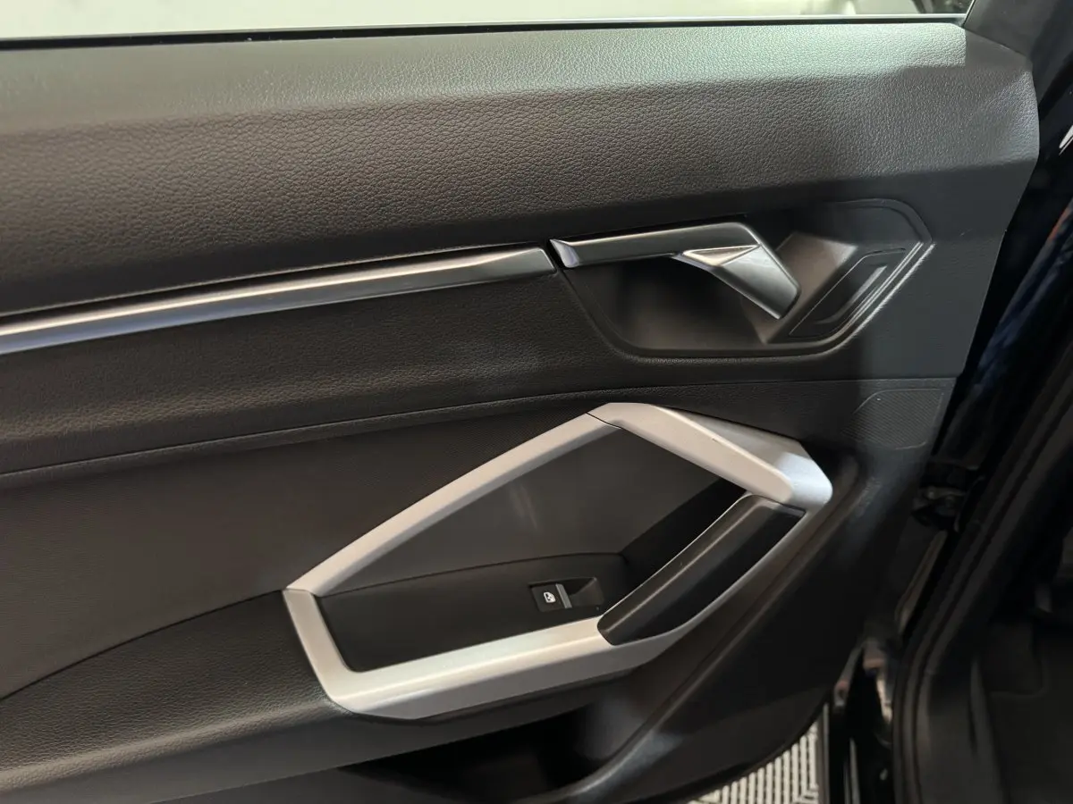 Vue rapprochée de la porte avant droite noire de l'Audi Q3 35 TFSI 2022 avec poignée argentée et bouton de verrouillage.