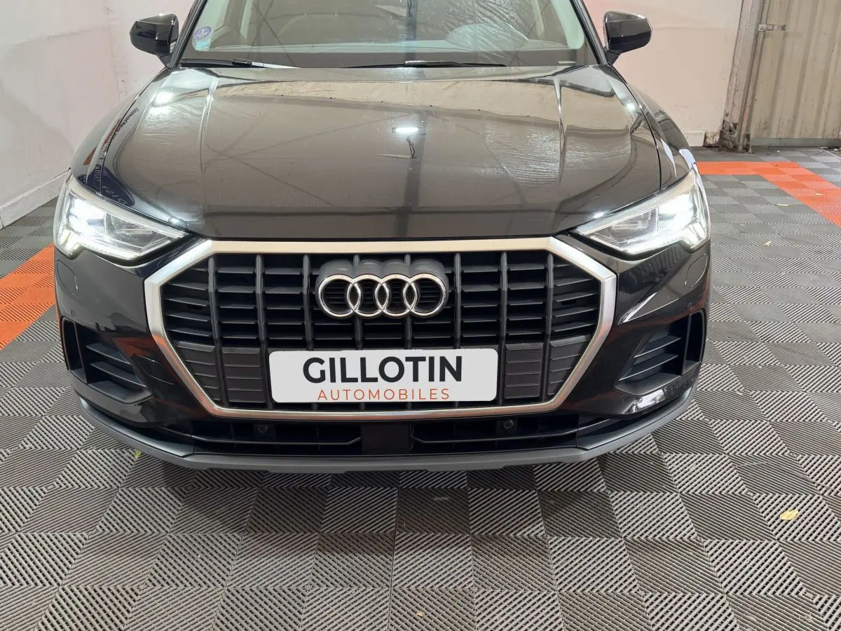 Vue avant d’un Audi Q3 noir 2022 avec calandre hexagonale et phares LED allumés dans un garage.