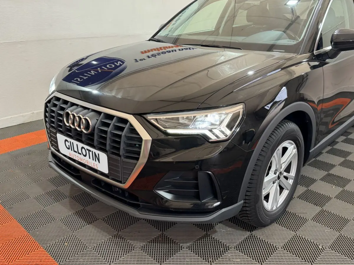 Vue 3/4 avant droit d'un Audi Q3 noir avec calandre hexagonale et phares LED allumés en intérieur showroom.