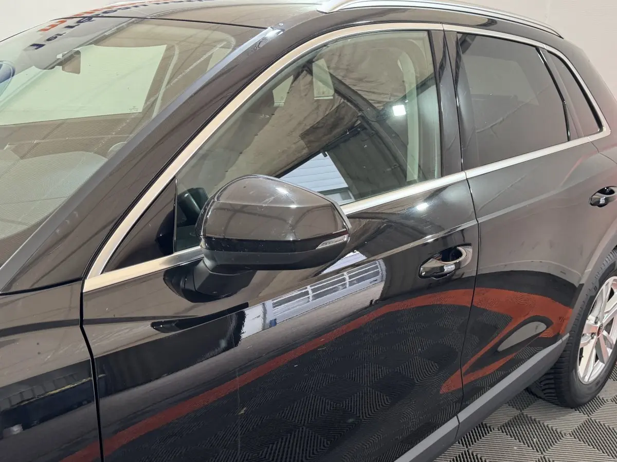 Vue latérale côté gauche d’un Audi Q3 noir 2022 avec rétroviseur et poignées de porte chromées.