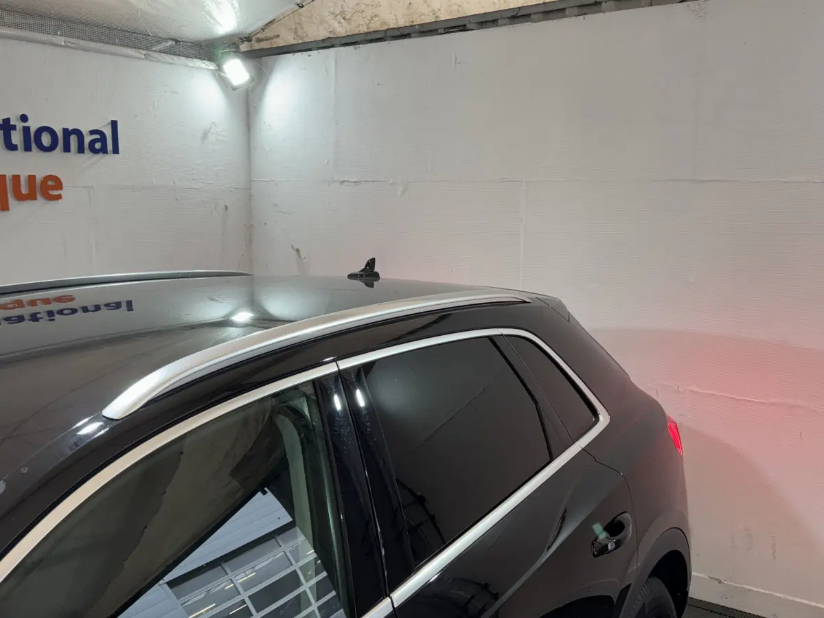 Vue latérale arrière droite d’un Audi Q3 noir avec vitres teintées et barres de toit chromées dans un garage.