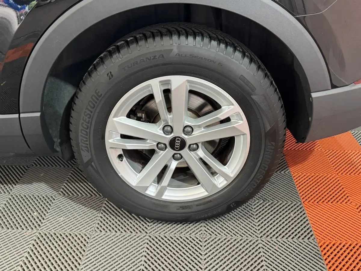 Gros plan sur la roue avant droite d’un Audi Q3 noir, mettant en valeur la jante argentée et le pneu Bridgestone.