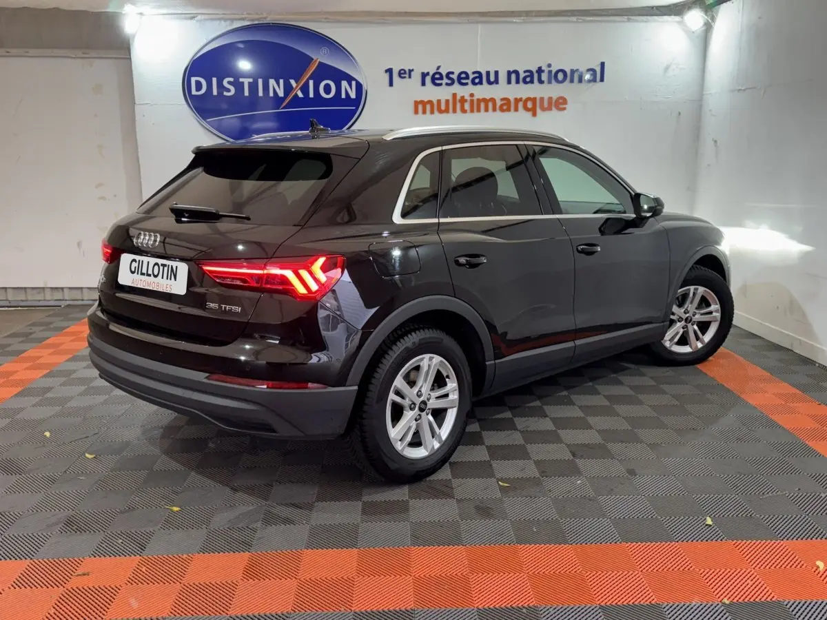 Audi Q3 noir vue 3/4 arrière droit avec feux arrière LED allumés dans un showroom intérieur.