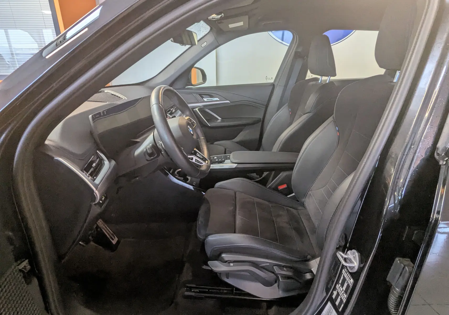 Intérieur noir côté conducteur du BMW X1 2025, sièges M Alcantara, volant cuir M et tableau de bord luxe visible.