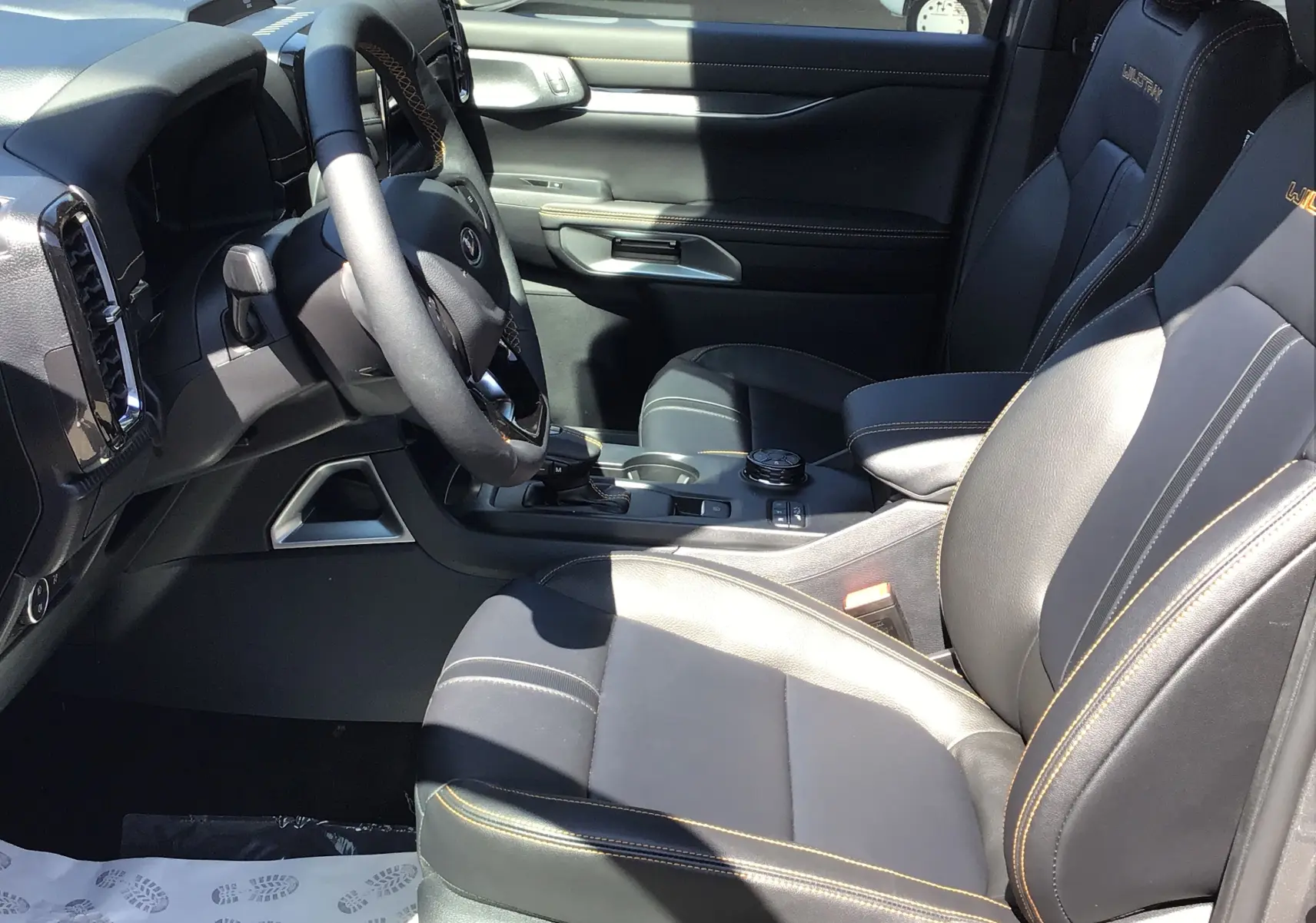 Intérieur côté conducteur du Ford Ranger Wildtrak 2025 en cuir noir avec surpiqûres orange et console centrale moderne.