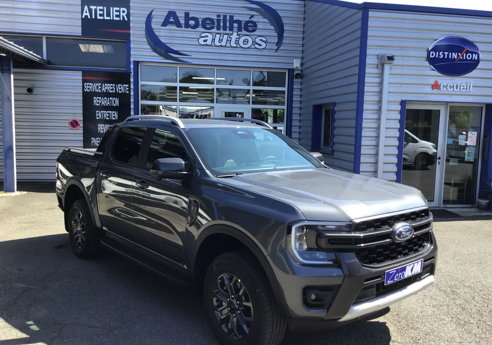Ford Ranger Double Cabine gris carbone vu en 3/4 avant droit, avec calandre noire et jantes foncées, devant un garage.