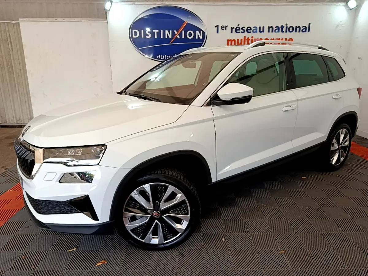 Vue 3/4 avant droite d'un Skoda Karoq blanc 2023 avec jantes alliage et barres de toit chromées.