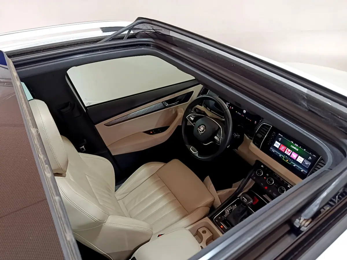 Vue plongeante sur l'intérieur beige et noir du Skoda Karoq 2023, avec tableau de bord digital et toit ouvrant.