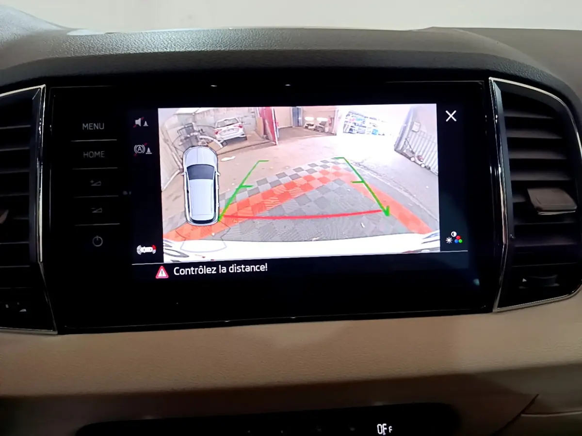 Écran tactile central montrant la caméra de recul avec alertes de distance du Skoda Karoq blanc, vue intérieure avant.
