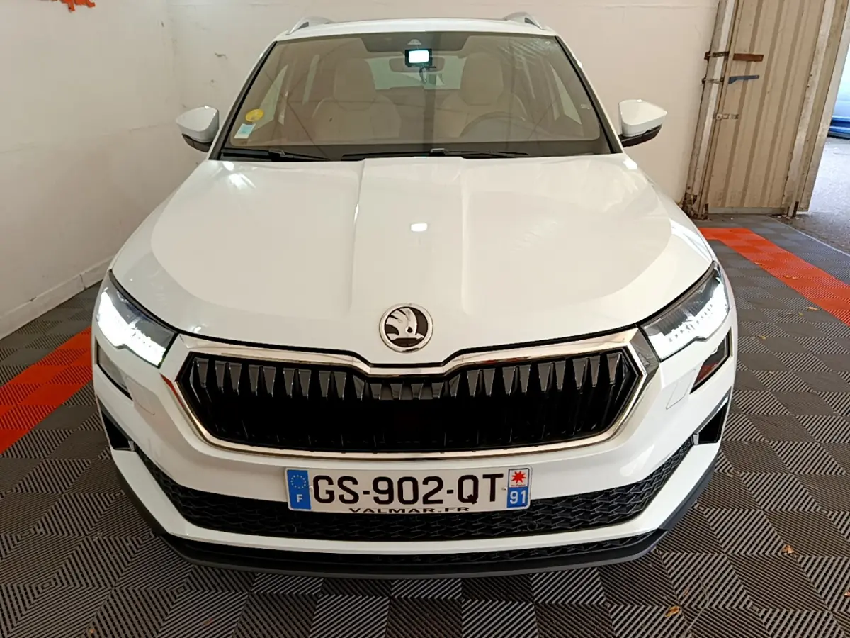 Vue avant d'un Skoda Karoq blanc 2023 avec calandre noire et phares LED allumés en intérieur.