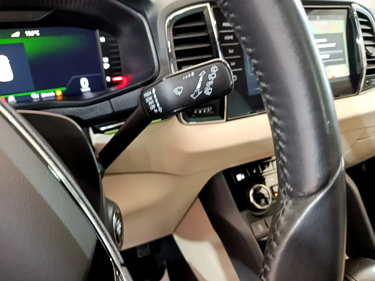 Vue rapprochée du volant noir et du tableau de bord beige du Skoda Karoq blanc, avec commandes au volant et écran tactile visible.