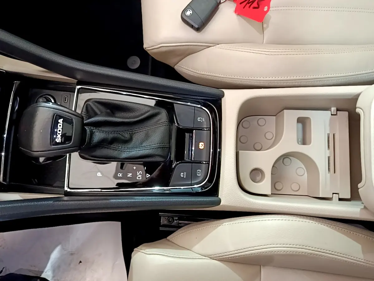 Vue plongeante sur la console centrale beige du Skoda Karoq 2023 avec levier de vitesse DSG noir et porte-gobelets intégré.