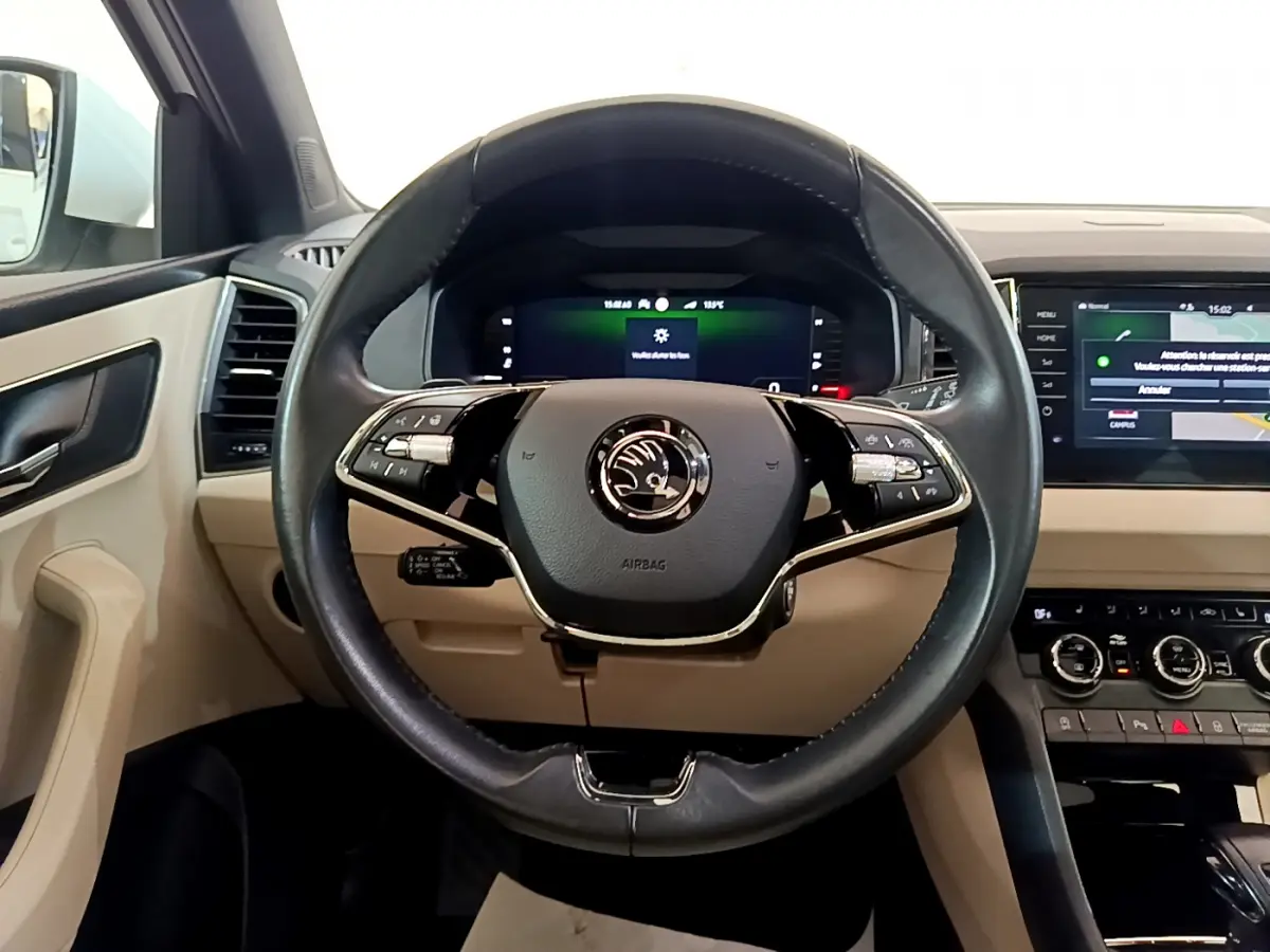 Vue frontale du volant cuir noir et du tableau de bord beige du Skoda Karoq 2023 avec écran tactile et affichage numérique.