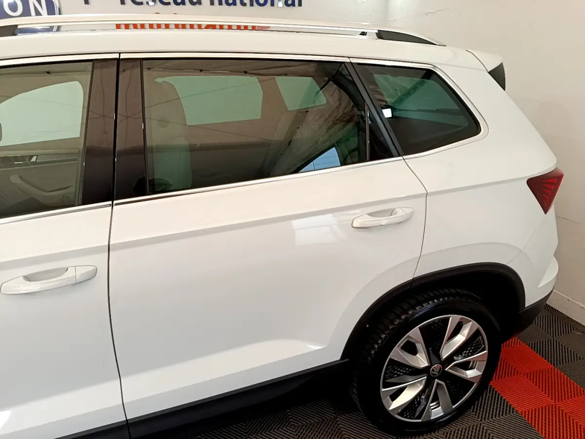 Vue latérale droite du Skoda Karoq blanc 2023, mettant en valeur la porte arrière et la roue arrière au design moderne.