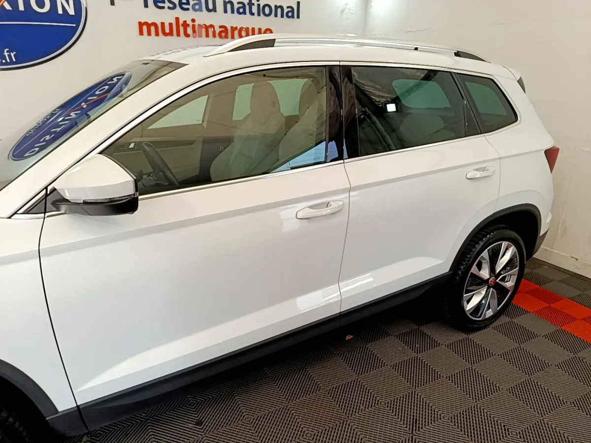 Vue de profil côté gauche du SUV blanc Skoda Karoq 2023 avec jantes alliage et vitres teintées.