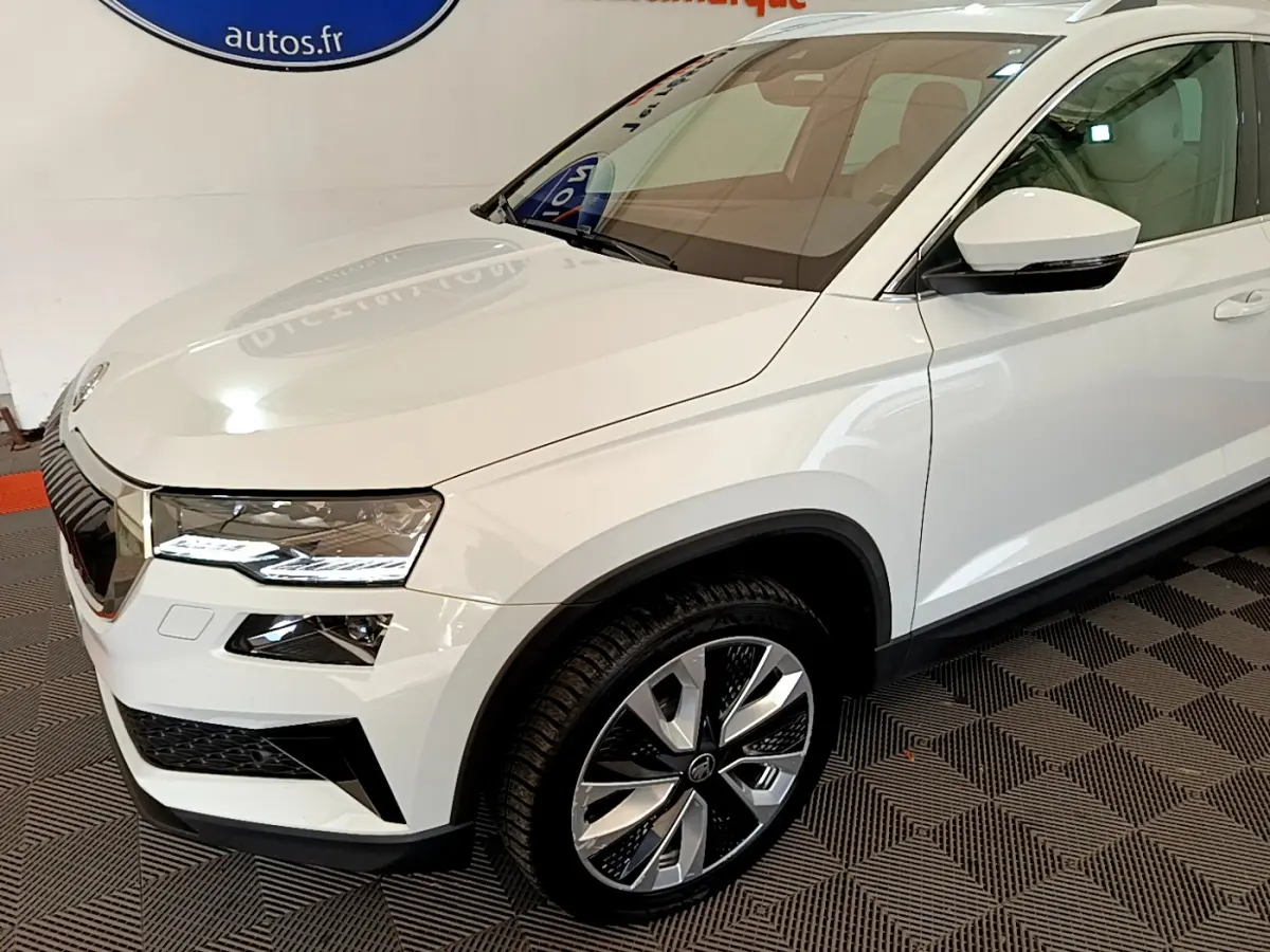 Vue 3/4 avant droit d'un Skoda Karoq blanc avec jantes alliage bicolores et phares LED ellipsoïdaux.