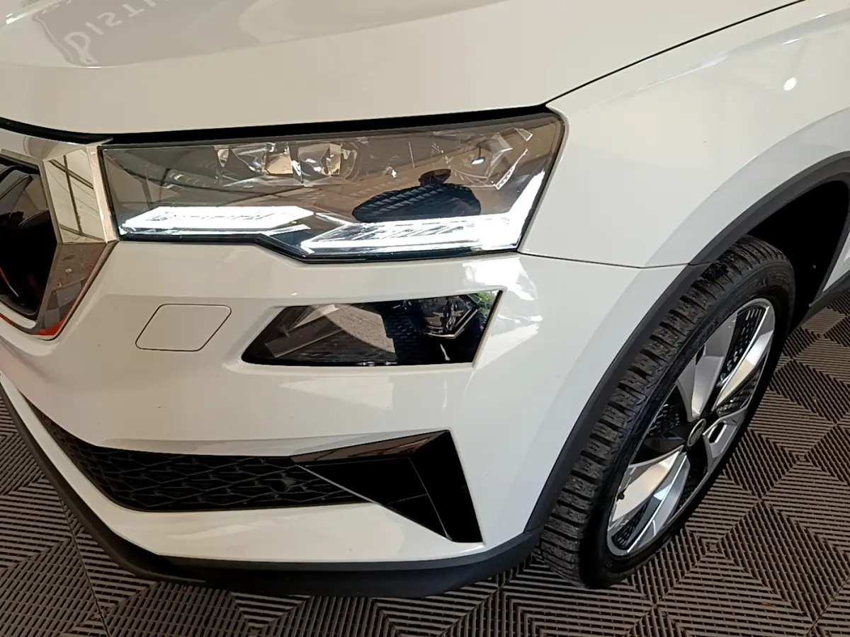 Gros plan sur l'avant droit blanc du Skoda Karoq 2023, mettant en valeur le phare LED et la jante alliage.
