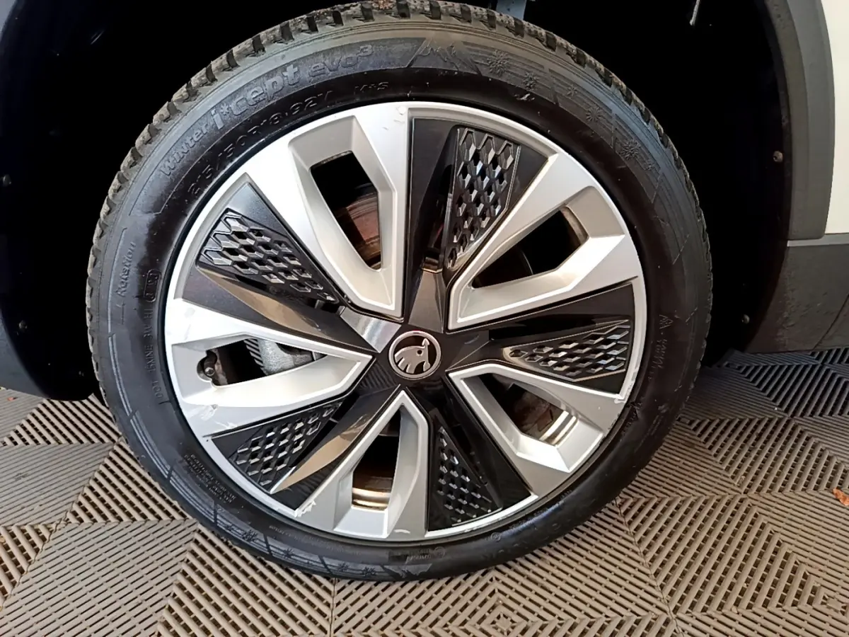 Gros plan sur la roue avant droite du Skoda Karoq blanc, mettant en valeur la jante alliage bicolore au design moderne.