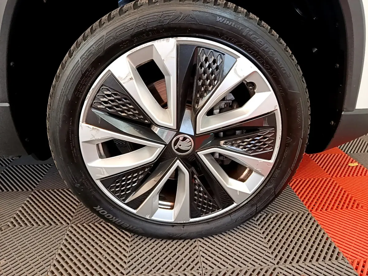 Gros plan sur la roue avant droite du Skoda Karoq blanc, mettant en valeur la jante alliage bicolore au design géométrique.