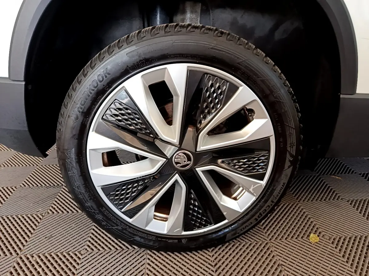 Gros plan sur la roue avant droite d’un Skoda Karoq blanc, jante alliage au design géométrique noir et argent.