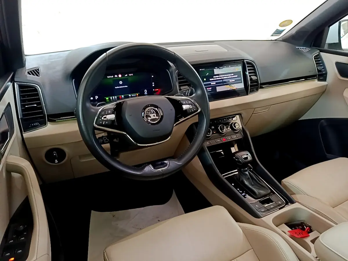 Vue intérieure avant droite du Skoda Karoq blanc, tableau de bord beige avec écran tactile et volant cuir noir.